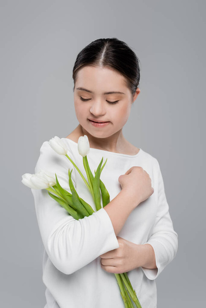 Woman with down syndrome holding white tulips isolated on grey  - Zdjęcie, obraz