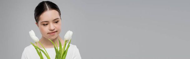 Mujer con síndrome de Down mirando flores blancas aisladas en gris, pancarta  - Foto, Imagen