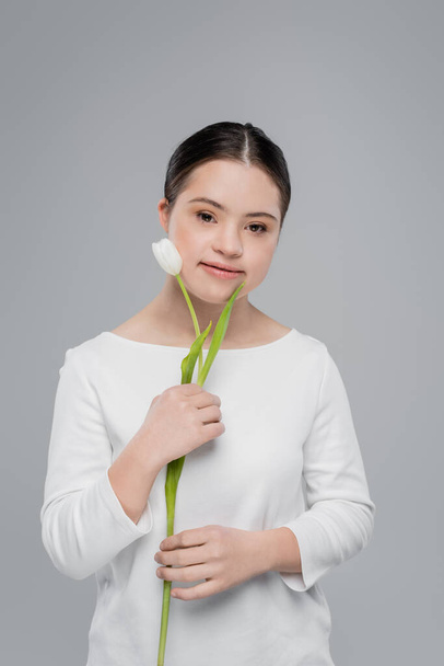 Young woman with down syndrome holding white tulip isolated on grey  - Φωτογραφία, εικόνα