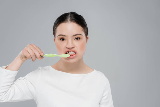 Woman with down syndrome brushing teeth isolated on grey  - Foto, Imagem