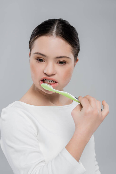 Bruna donna con sindrome di Down lavarsi i denti isolato su grigio  - Foto, immagini
