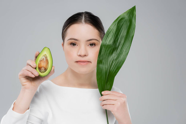 Woman with down syndrome holding leaf and avocado isolated on grey  - Φωτογραφία, εικόνα