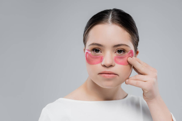 Jeune femme atteinte du syndrome du duvet appliquant des patchs oculaires isolés sur gris  - Photo, image