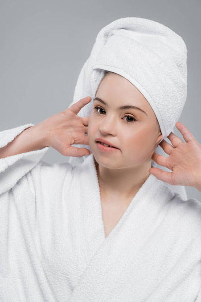 Woman with down syndrome in bathrobe touching towel on head isolated on grey  - Foto, afbeelding