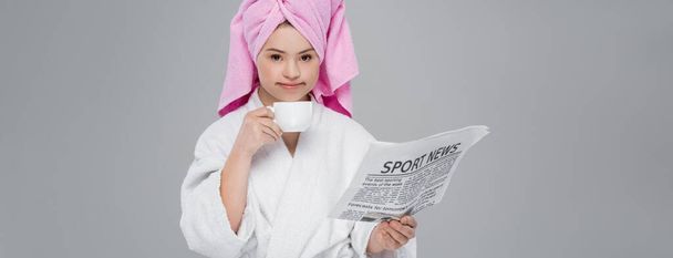 Женщина с синдромом Дауна в халате держит спортивные новости и кубок изолированы на серый, баннер  - Фото, изображение