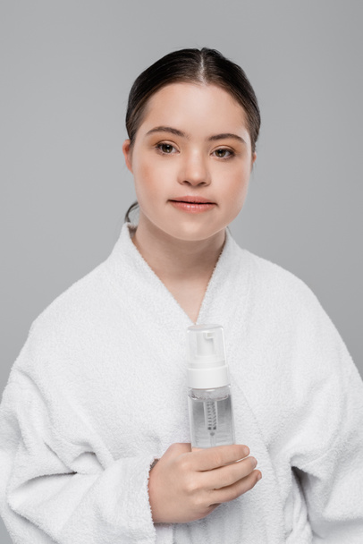 Жінка з синдромом Дауна в халаті тримає піну для очищення ізольовано на сірому
  - Фото, зображення