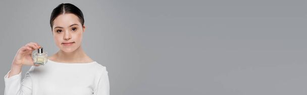 Brunette vrouw met dons syndroom in blouse houden parfum geïsoleerd op grijs, banner  - Foto, afbeelding