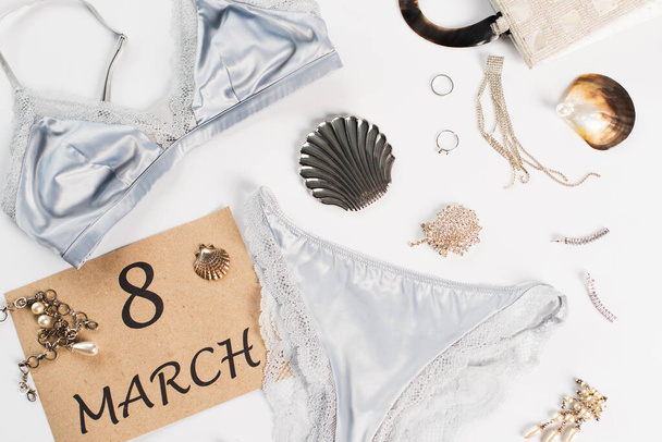 Top view of lingerie near bag and card with 8 march lettering on white background  - 写真・画像
