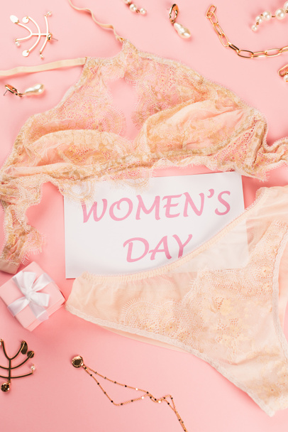 Top view of card with womens day lettering near lingerie, gift box and accessories on pink background  - Fotó, kép