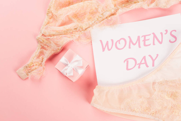 Draufsicht auf Karte mit Schriftzug zum Frauentag in der Nähe von Dessous und Geschenk auf rosa Hintergrund  - Foto, Bild