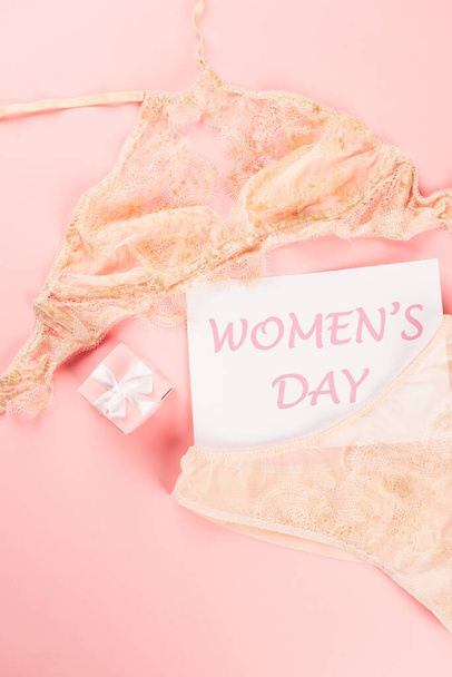 Vista superior de la ropa interior, regalo y tarjeta con letras de día para mujer sobre fondo rosa  - Foto, imagen