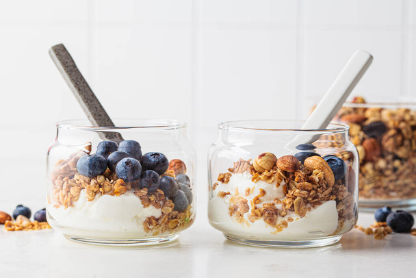 Granola with nuts, yogurt and berries in a jar. Breakfast parfait with muesli, yoghurt and blueberries, white kitchen background. - Photo, image