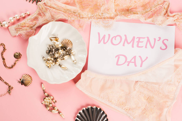 Top view of card with womens day lettering near lace lingerie and accessories on pink background  - Photo, Image