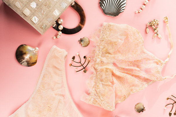 Top view of lace lingerie near golden accessories and bag on pink background  - Fotó, kép