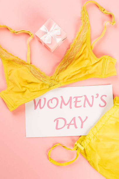 Top view of bra, card with womens day lettering and gift on pink background  - Fotoğraf, Görsel