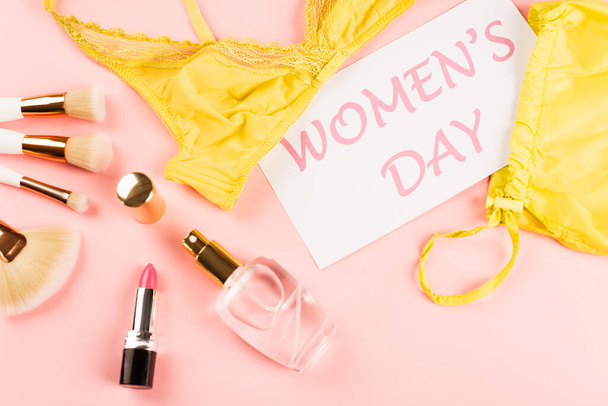Draufsicht auf BH-nahe Karte mit Schriftzug zum Frauentag, Parfüm und Kosmetikpinseln auf rosa Hintergrund  - Foto, Bild