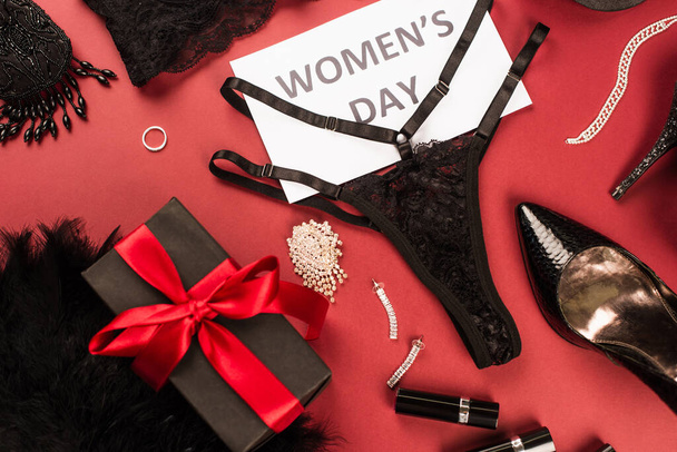 Vista superior de la ropa interior de encaje, tarjeta con letras de día para mujer cerca del regalo y tacones sobre fondo rojo  - Foto, imagen
