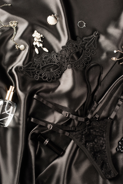 Top view of sexual mask, panties and perfume on black satin background - Φωτογραφία, εικόνα