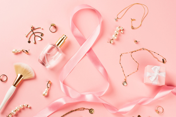 Draufsicht auf Accessoires, Parfüm und Schleife in Form von 8 Zeichen auf rosa Hintergrund  - Foto, Bild