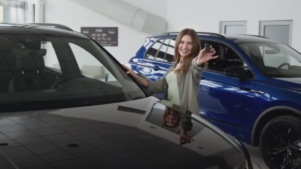 Młoda kobieta sukcesu zakupu nowego samochodu w salonie dealerskim, pozowanie z kluczy w pobliżu nowego samochodu, śledzenie strzał - Materiał filmowy, wideo