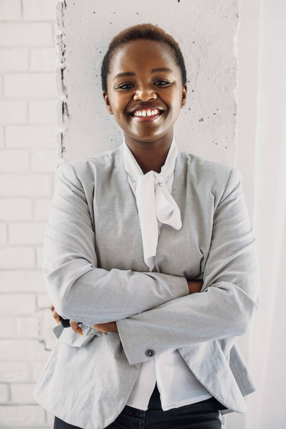 Porträt einer afrikanisch-amerikanischen Frau, die mit gefalteten Händen vor einer weißen Wand posiert und in die Kamera lächelt. Weißer Hintergrund. Geschäftsfrau. - Foto, Bild