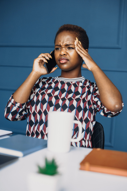 Afrikkalainen amerikkalainen nainen puhuu älypuhelimella istuu pöydällä korosti uudessa työssään. Liikenaisen muotokuva. Puhuvat ihmiset. - Valokuva, kuva