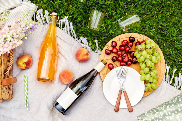 food, drinks and basket on picnic blanket on grass - Photo, Image