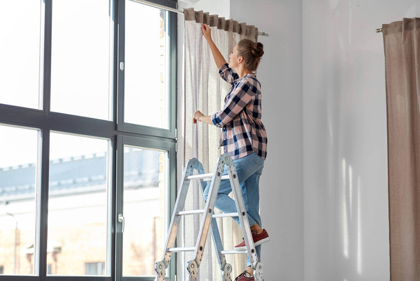 vrouw op ladder gordijnen opknoping thuis - Foto, afbeelding