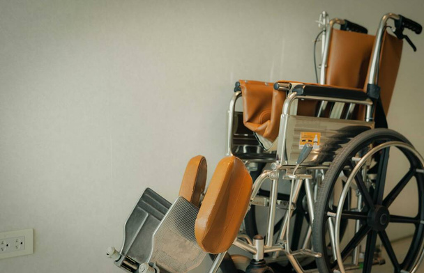 Pusty wózek inwalidzki w pobliżu ściany w szpitalu dla pacjentów służby i osób niepełnosprawnych. Sprzęt medyczny w szpitalu do pomocy starszym ludziom. Krzesło z kołami do opieki nad pacjentem w domu opieki. - Zdjęcie, obraz