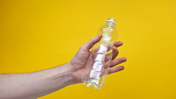 przycięty widok człowieka trzymającego plastikową butelkę izolowaną na żółto  - Zdjęcie, obraz