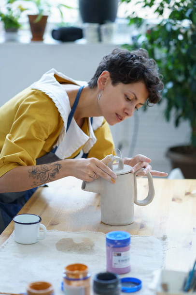 Young woman in apron learning how to make ceramics during masterclass in pottery workshop - Photo, Image