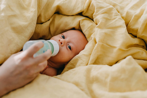 Biberon mère nourrissant le nouveau-né couché au lit recouvert d'une grande couverture jaune. - Photo, image