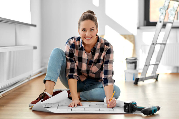 woman with blueprint sitting on floor at home - Zdjęcie, obraz