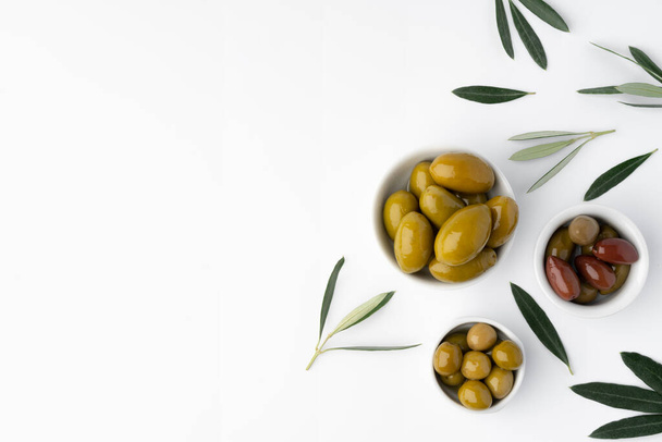 Bowl with green olives and olive leaves on white background - Φωτογραφία, εικόνα