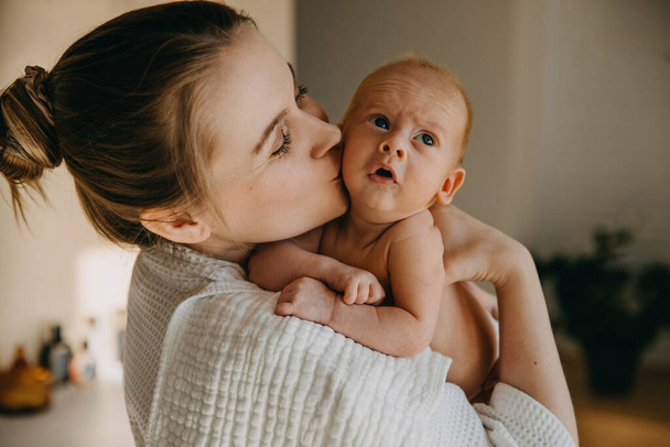 Η μητέρα φιλάει ένα μωρό ενός μήνα στο μάγουλο. - Φωτογραφία, εικόνα