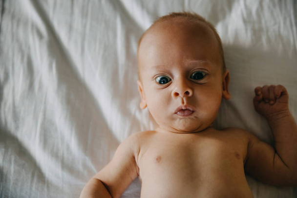 Портрет крупным планом серьезного ребенка месячной давности, лежащего в постели. - Фото, изображение