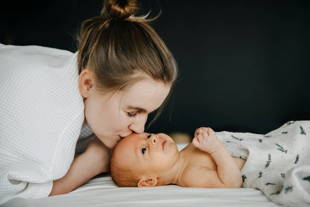 Μητέρα που φιλάει ένα μωρό ενός μήνα στο μέτωπο, ξαπλωμένη στο κρεβάτι. - Φωτογραφία, εικόνα