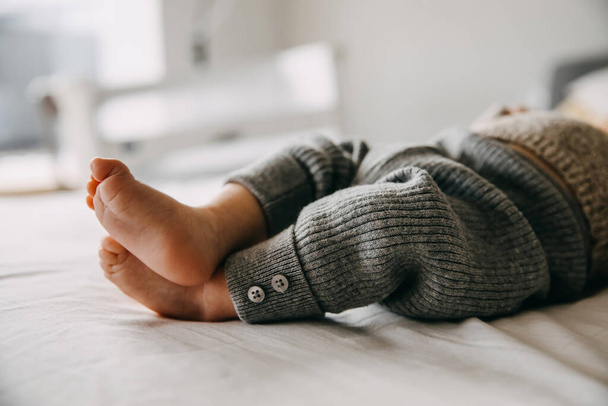 Closeup of baby barefoot feet in grey knitted wool pants.  - 写真・画像