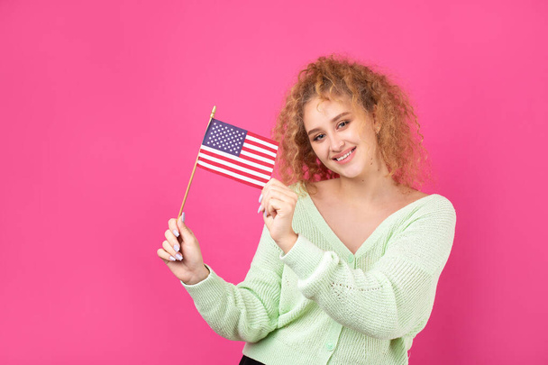 Μια νεαρή ευτυχισμένη κοπέλα με ένα χαμόγελο στο πρόσωπό της κρατά μια αμερικανική σημαία στα χέρια της. Σύμβολο πατριωτισμού και ελευθερίας. - Φωτογραφία, εικόνα