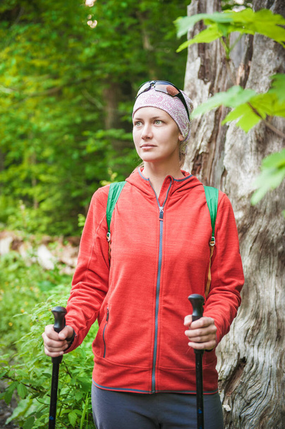 Mujer excursionista en la chaqueta roja con palos en el bosque al aire libre. Concepto turístico - Foto, imagen