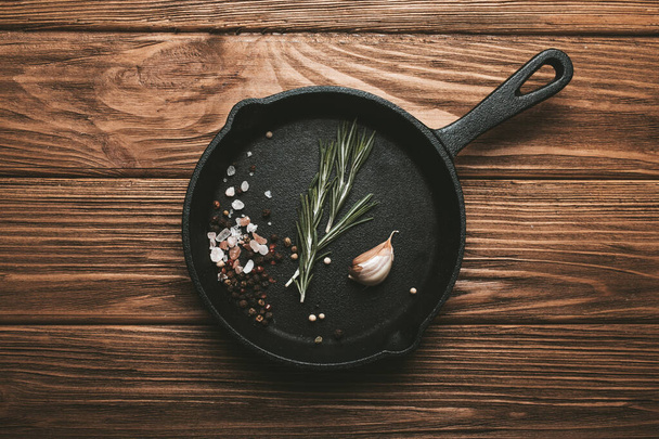 Black cast iron frying pan skillet with food cooking ingredients fresh rosemary, garlic, salt and pepper - Foto, Imagen