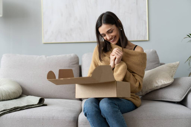 Happy young woman sit on couch room unpack cardboard box buying goods on Internet. shopping online, delivery concept - Фото, изображение