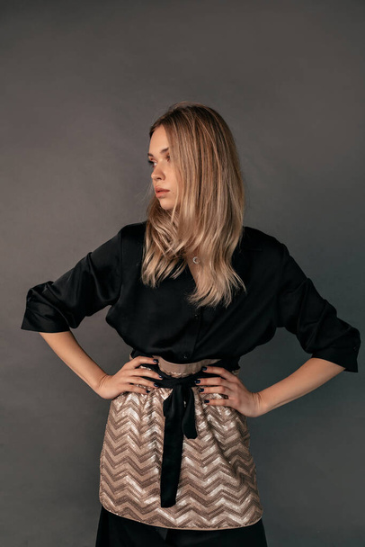 Studio portrait of fashionable stylish woman with blond hair wearing black with gold dress posing at studio over grey background. High quality photo - Φωτογραφία, εικόνα