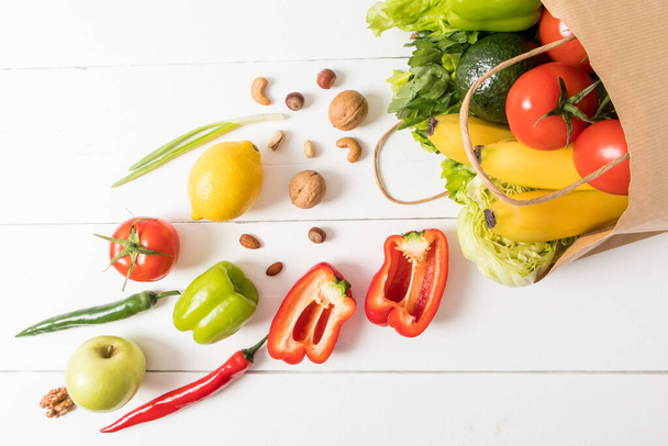 top view of the white wooden background with a full paper bag of fruits and vegetables. the concept of proper food, delivery from the supermarket - Foto, imagen