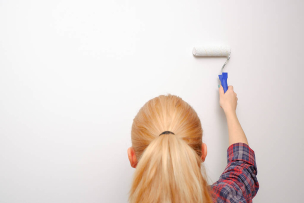 Pintura interior de la casa. Mujer pintando pared de sala de estar con rodillo de pintura. Vista desde la parte posterior a la mano con la herramienta. - Foto, imagen