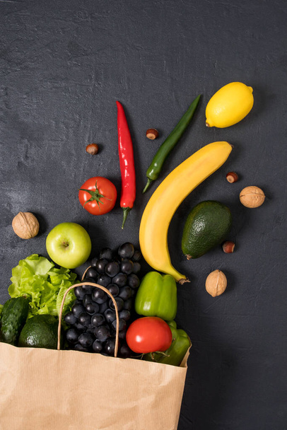 Kraft paper bag filled with fresh vegetables and fruits on a black background. the concept of proper healthy food, food selection - 写真・画像
