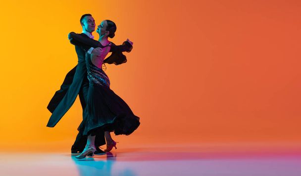 Flyer with dancing couple, beautiful man and woman dancing waltz isolated over gradient orange pink background in neon light. Beauty, art, sport concept - Foto, Imagen
