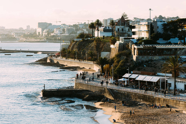 Cascais, Portugal - February 5, 2022: High perspective view of people at the promenade at Poca Beach, a small, sandy urban beach with rocky areas with cafes - Foto, Imagen