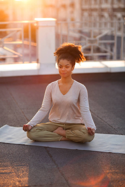 Cropped photo of  woman sitting in lotus pose on mat and practicing yoga, female doing namaste gesture while meditating outdoors. Meditation and mindfulness concept - Foto, Bild