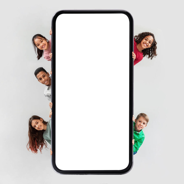 Diverse Kinder posieren neben riesigem Handy-Bildschirm vor grauem Hintergrund - Foto, Bild